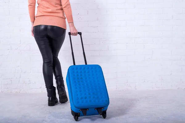 A woman with a blue suitcase near a white brick wall, copy space. — Stock Photo, Image
