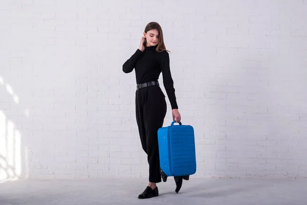 Meisje staat met een blauwe koffer in de buurt van een witte bakstenen muur. Vrije ruimte. — Stockfoto