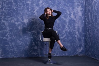 Genç bir kadın mavi bir duvarın arka planına karşı bir bar taburesinde oturuyor, boş alan.