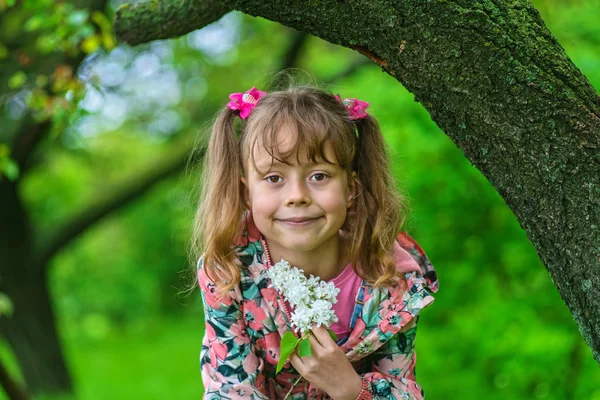 Una niña sonriente de unos 6 años con una ramita de lilas en las manos . — Foto de Stock