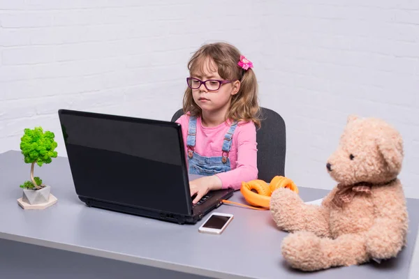 Niña en gafas con un portátil. Una chica jugando un videojuego en un portátil . — Foto de Stock