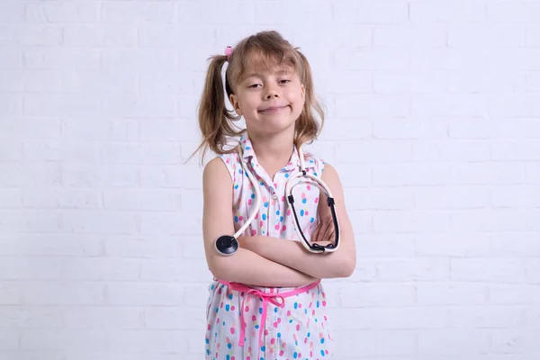 Retrato de una niña de unos 7 años con un estetoscopio contra una pared blanca, espacio libre para su texto . — Foto de Stock