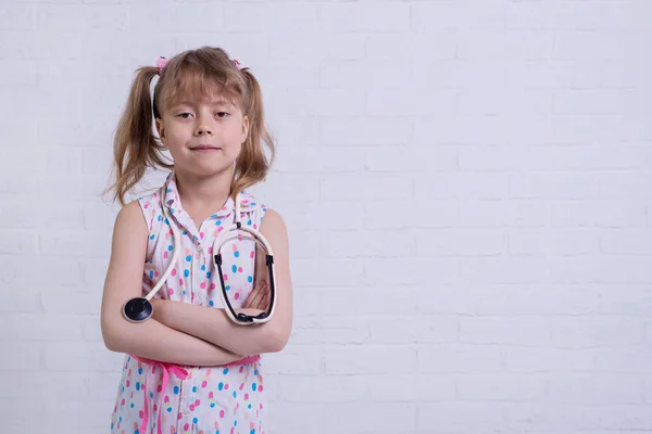 Портрет девушки около 7 лет со стетоскопом на белой стене, свободное место для текста . — стоковое фото