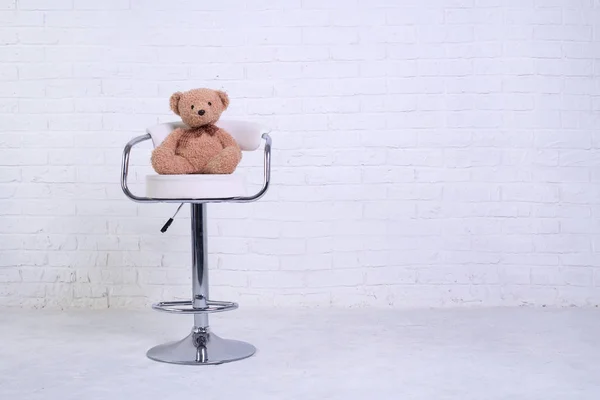 Nallebjörn sitter på en stol mot bakgrund av en vit tegelvägg, ledigt utrymme. — Stockfoto