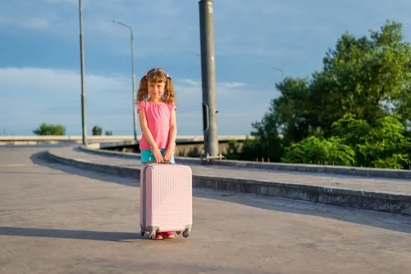 Kleines Mädchen mit rosa Koffer steht auf der Straße. — Stockfoto