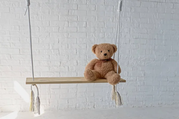 Nallebjörn på en gunga i studion på en bakgrund av vita tegel. — Stockfoto