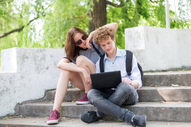 Genç bir çift bir dizüstü bilgisayar ile parkta merdivenlerde oturuyor.