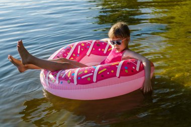 Şişme halkası olan pembe mayogiyen çocuk nehirde yüzüyor.
