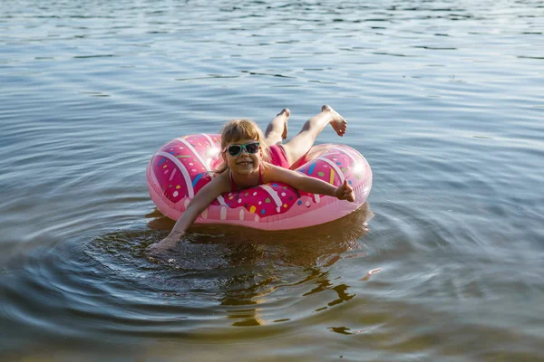 Chica en un traje de baño rosa y gafas de sol nadando en un anillo inflable, una copia del espacio libre . — Foto de Stock