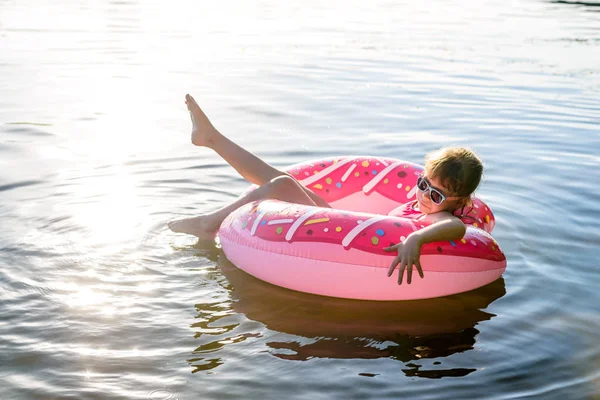Chica en un traje de baño rosa y gafas de sol nadando en un anillo inflable, una copia del espacio libre . — Foto de Stock