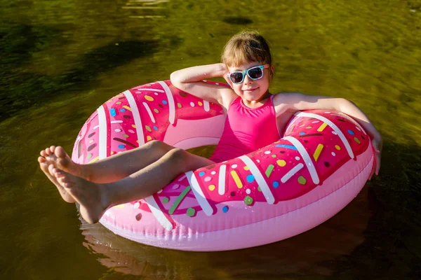 Chica en un traje de baño rosa y gafas de sol nadando en un anillo inflable . — Foto de Stock