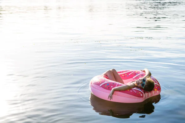 Chica en un traje de baño rosa y gafas de sol nadando en un anillo inflable, una copia del espacio libre . — Foto de Stock