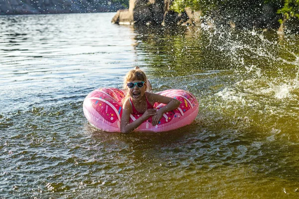 Criança em um maiô rosa com um anel inflável nada no rio . — Fotografia de Stock