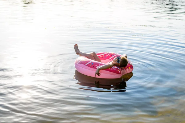 Jenta i rosa badedrakt og solbriller som svømmer på en oppblåsbar ring, en kopi av det ledige rommet . – stockfoto