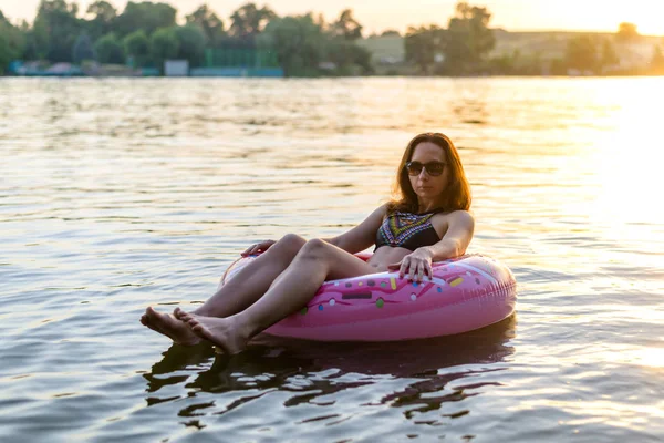 Jeune femme détend la natation sur un beignet gonflable dans la rivière dans le contexte du coucher du soleil . — Photo