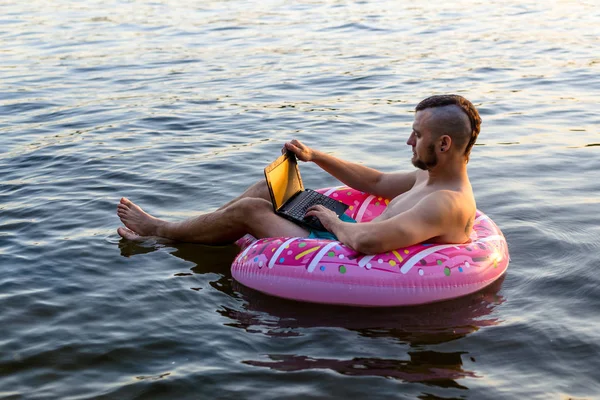 Hombre adicto al trabajo que trabaja en un ordenador portátil mientras está sentado en un anillo inflable, espacio de copia . — Foto de Stock