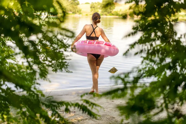 Jeune femme va nager avec un anneau gonflable, vue arrière . — Photo