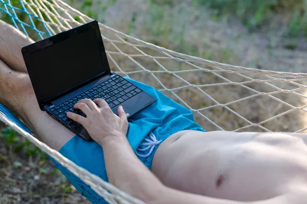Freelancer trabajando en un portátil tumbado en una hamaca . — Foto de Stock