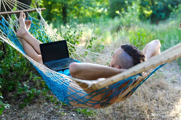 Freelancer trabajando en un portátil tumbado en una hamaca . — Foto de Stock