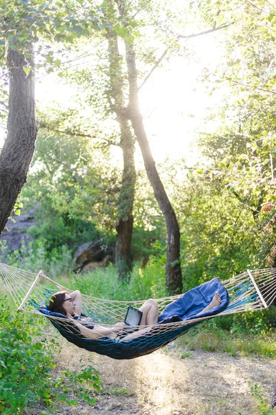 Femme d'affaires travaillant sur ordinateur portable pendant les vacances. Jeune femme couchée dans un hamac et regardant vers un ordinateur portable . — Photo