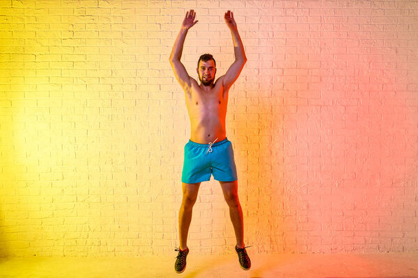 Young sporty man performs a jump on a yellow background.
