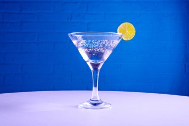 Martini bardağındaki vermut ve mavi arka planda bir dilim kireç, kopya alanı.