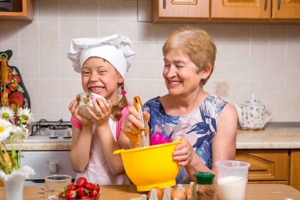 Großmutter und kleine Enkelin bereiten den Teig für den Kuchen zu. — Stockfoto
