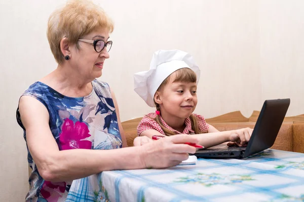 Η γιαγιά και η εγγονή σε ένα καπέλο σεφ αναζητούν συνταγές στο διαδίκτυο. — Φωτογραφία Αρχείου