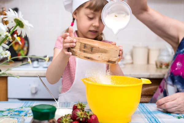 Großmutter und kleine Enkelin bereiten den Teig für den Kuchen zu. — Stockfoto