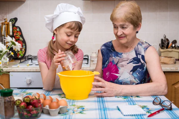 Grandmother and little granddaughter prepare the dough for the cake. — Stock Photo, Image