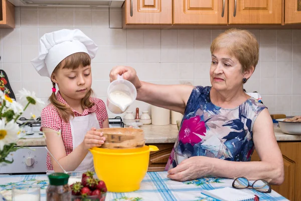 Großmutter und kleine Enkelin bereiten den Teig für den Kuchen zu. — Stockfoto