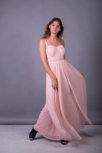 Молода дівчина в рожевій сукні позує на сірому фоні . — стокове фото