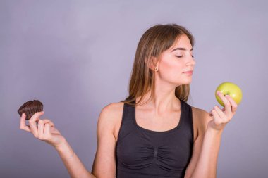 Doğru seçim. Bir elinde yeşil elma ve başka bir pasta tutan spor giyim genç fitness kadın Studio çekim.
