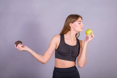 Doğru seçim. Bir elinde yeşil elma ve başka bir pasta tutan spor giyim genç fitness kadın Studio çekim.