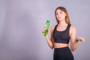 Gri stüdyo arka plan üzerinde tatlı su bir şişe tutan ince genç kadın.