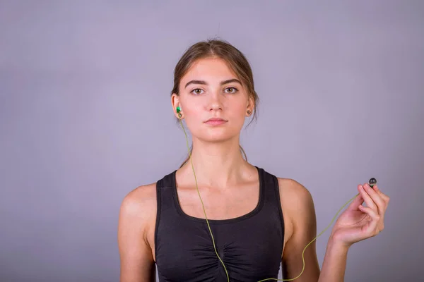 Portrait of young woman listening to music using earphones and smartphone in studio on gray background. — Stock Photo, Image