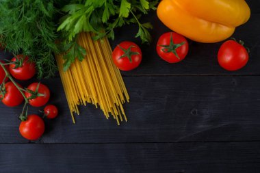 Ahşap bir masa üstü görünümünde kuru makarna ve sebze.