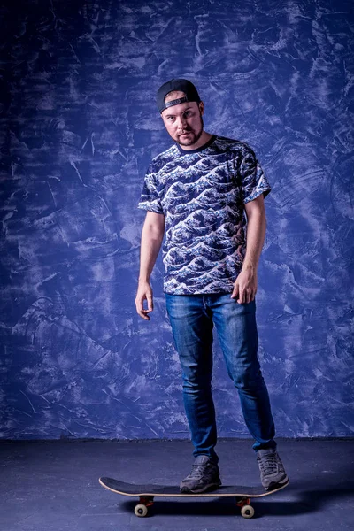 Mavi arka plan üzerinde bir kaykay üzerinde duran kaykaycı.