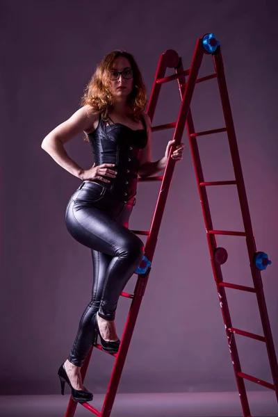 Sexy slanke vrouw in een korset en zwarte broek staat op een trapje. — Stockfoto