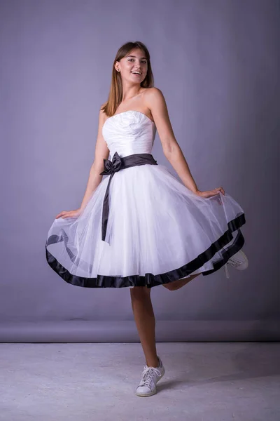 Joven modelo femenino hermoso en vestido blanco sobre fondo gris . — Foto de Stock