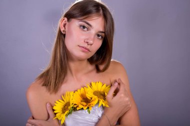 Gri bir arka plan üzerinde bir ayçiçeği çiçekleri tutan beyaz elbisegüzel kız.