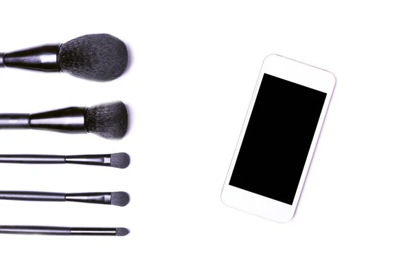 Cepillos de maquillaje profesionales y teléfonos inteligentes aislados en blanco a — Foto de Stock