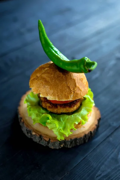 Homemade burger with hot pepper on a wooden black table.