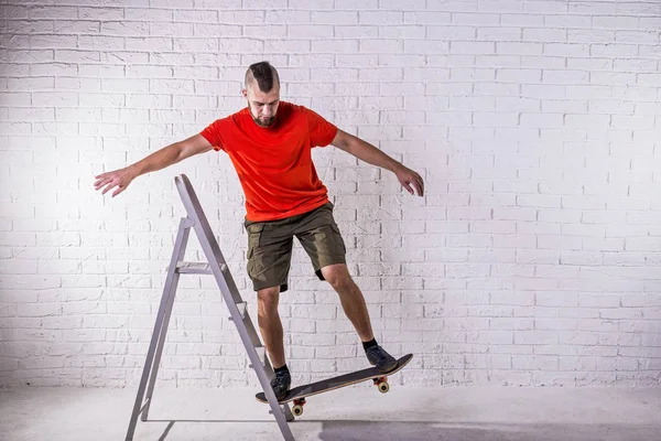 Skateboarder eseguire un trucco su uno skateboard sullo sfondo di una parete bianca . — Foto Stock