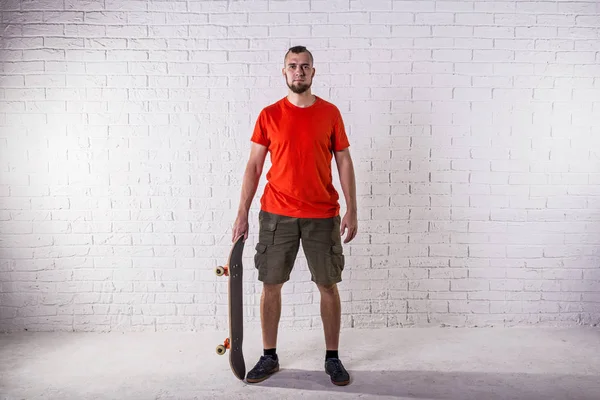 Skateboarder standing with skateboard on the background of a white wall. — Stock Photo, Image