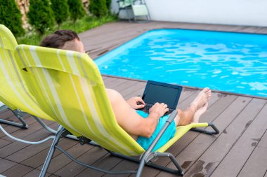 Havuzda takılan ve dizüstü bilgisayar kullanan bir adam. İşkolik, tatillerde çalışıyor..