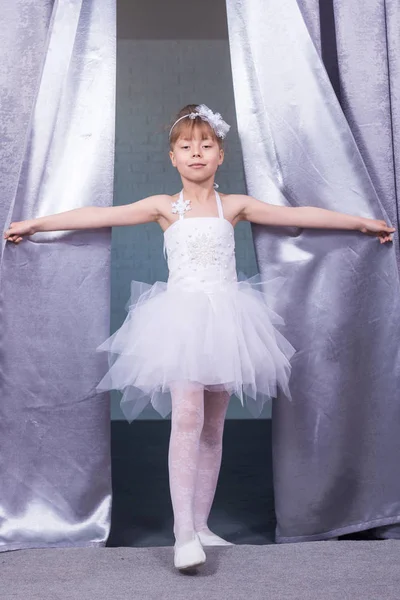 Niña linda en un vestido blanco mirando la escena debido a las cortinas . — Foto de Stock