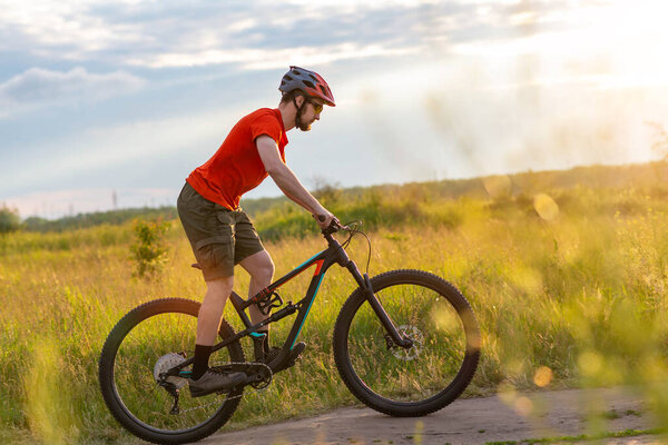 Велосипедист в ярко-оранжевой футболке катается на велосипеде по лугу во время заката. Концепция активного образа жизни. Велоспорт
.