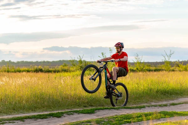 Rowerzysta Jasnopomarańczowej Koszulce Jeździ Tylnym Kole Roweru Wzdłuż Łąki Podczas — Zdjęcie stockowe