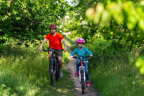 Dad and daughter ride bikes along a forest path, an active lifestyle. School break. Active family.